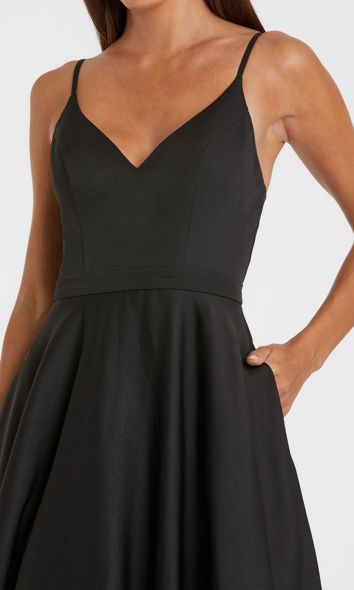 A woman wearing the Classic Long A-Line Formal Dress: Mac Duggal 48855 in black, featuring a sleeveless design, fitted bodice, and flared skirt, stands with one hand in her pocket.
